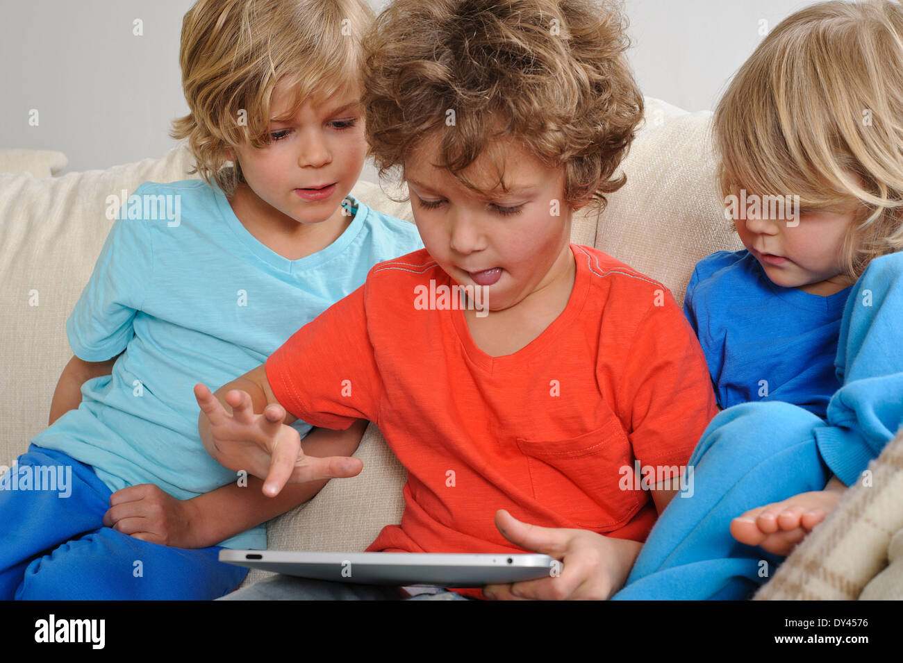 Ein ca. 8-9 Jahre alt spielt ein Spiel auf einem Touch-Screen-Tablette. Seine jüngeren Brüder beobachten jede Bewegung intensiv Stockfoto