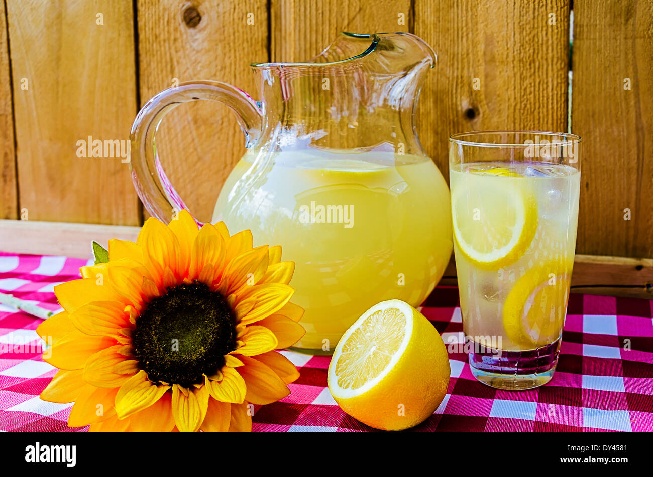 Limonade mit in Scheiben geschnittenen Zitronen, Krug und Sonnenblumen auf karierte Tischdecke. Stockfoto