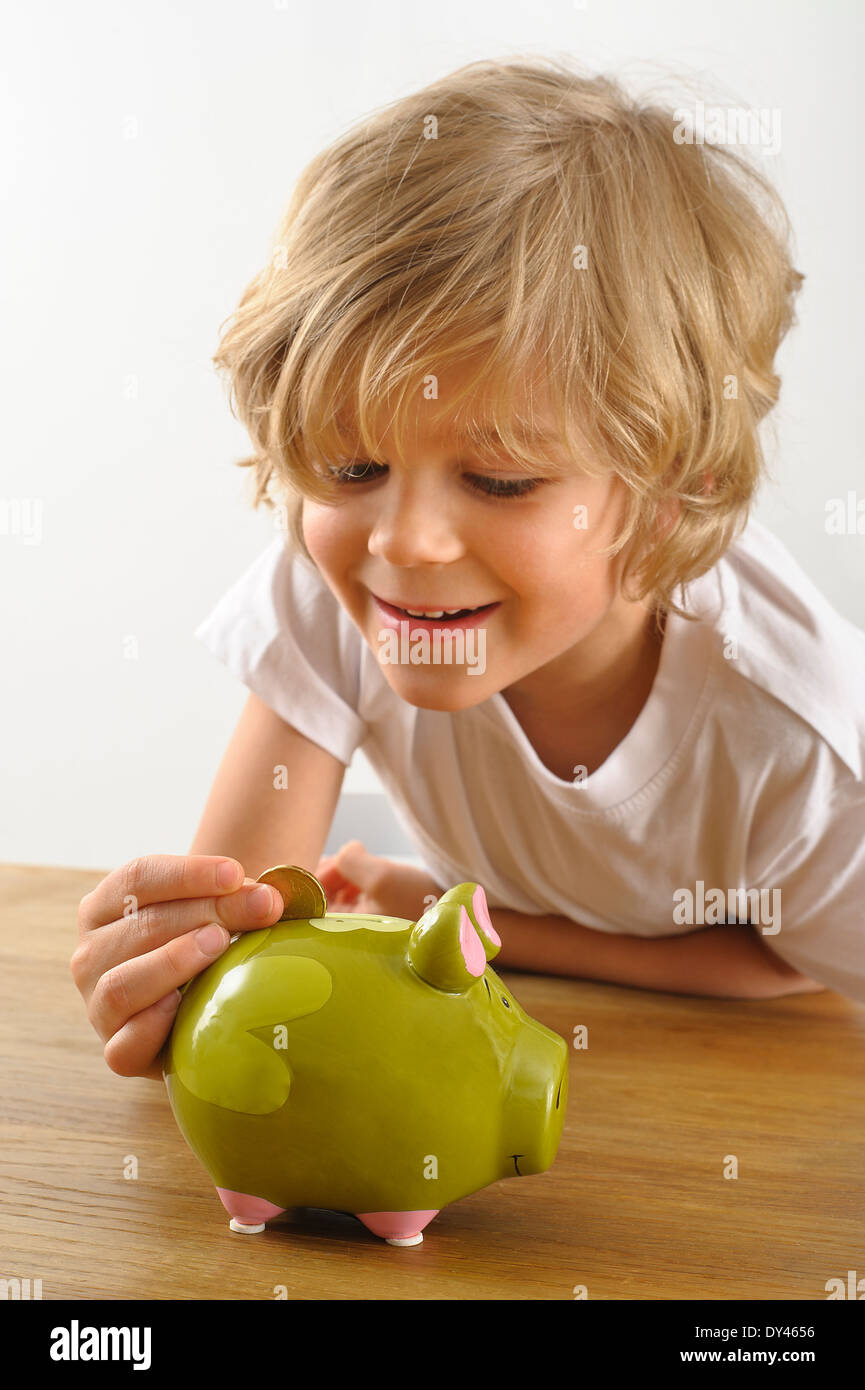 kleiner Junge legt eine Münze in sein Sparschwein Stockfoto