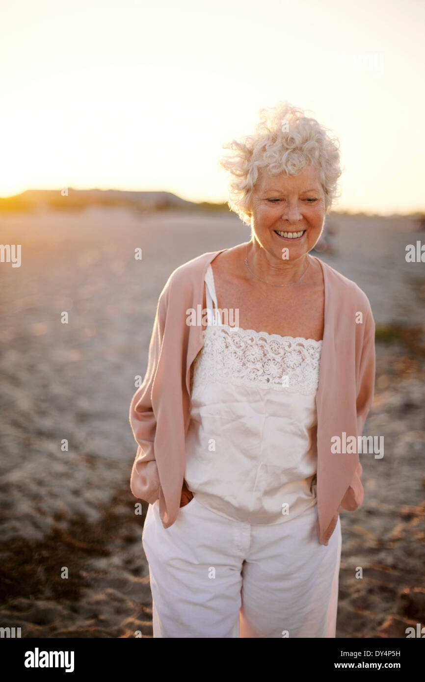 Porträt von glücklich Reife Frau zu Fuß am Strand. Schöne alte kaukasische Dame zu Fuß mit Lächeln auf Gesicht - im freien Stockfoto