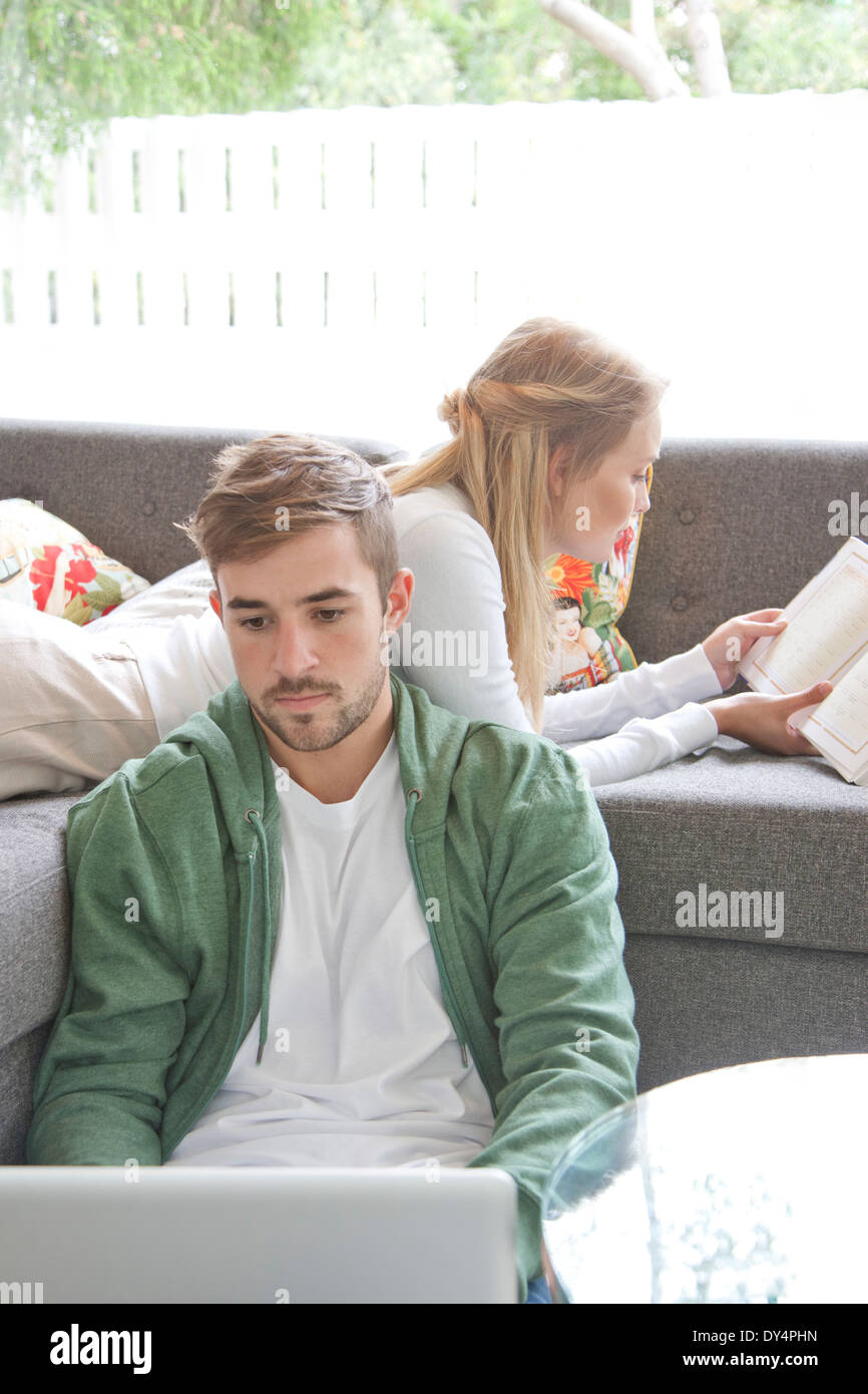 Mann mit Laptop und Frau liest Buch auf Sofa Stockfoto