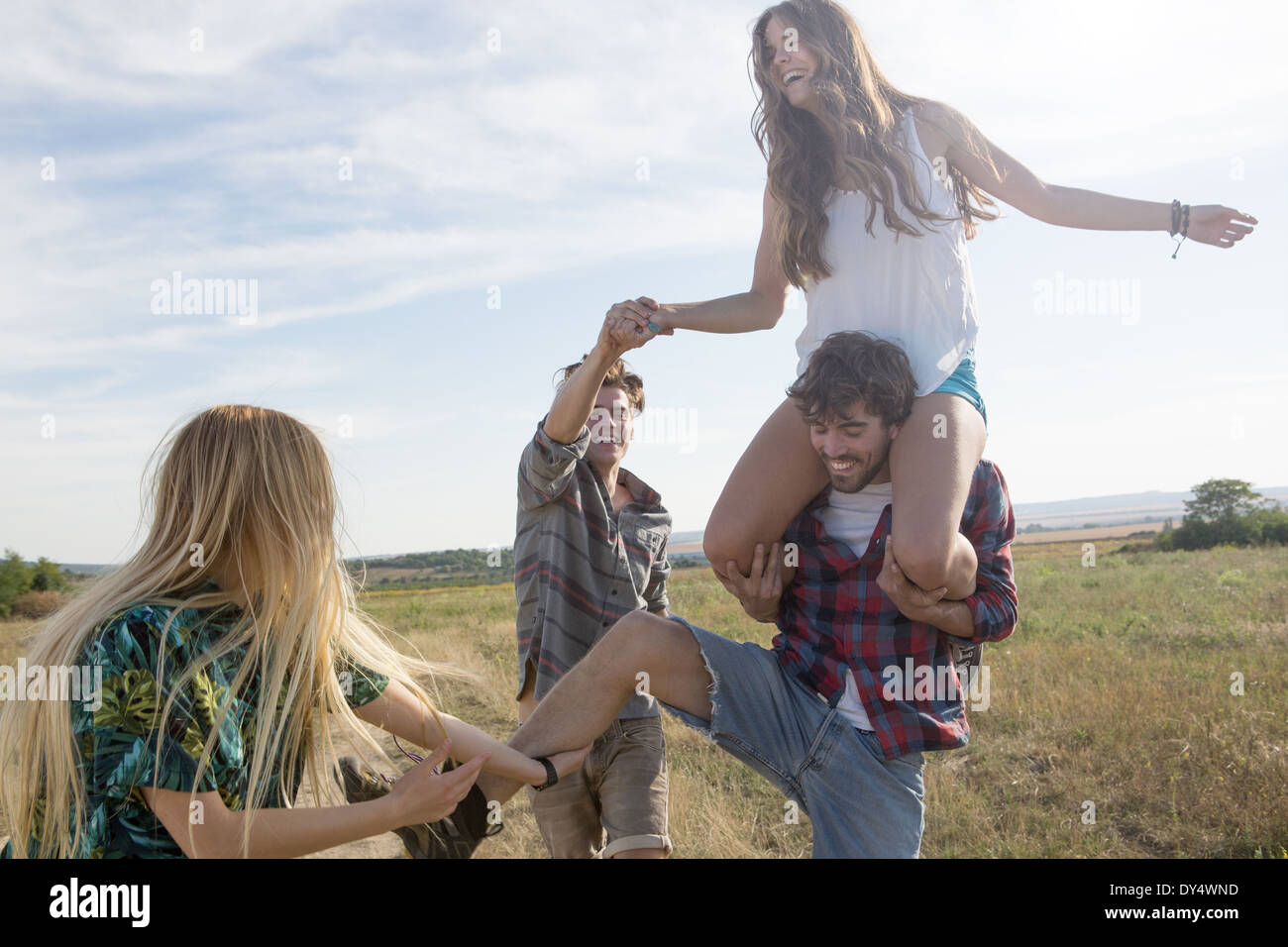 Vier Freunde spielen, Mann, die Frau auf den Schultern tragen Stockfoto
