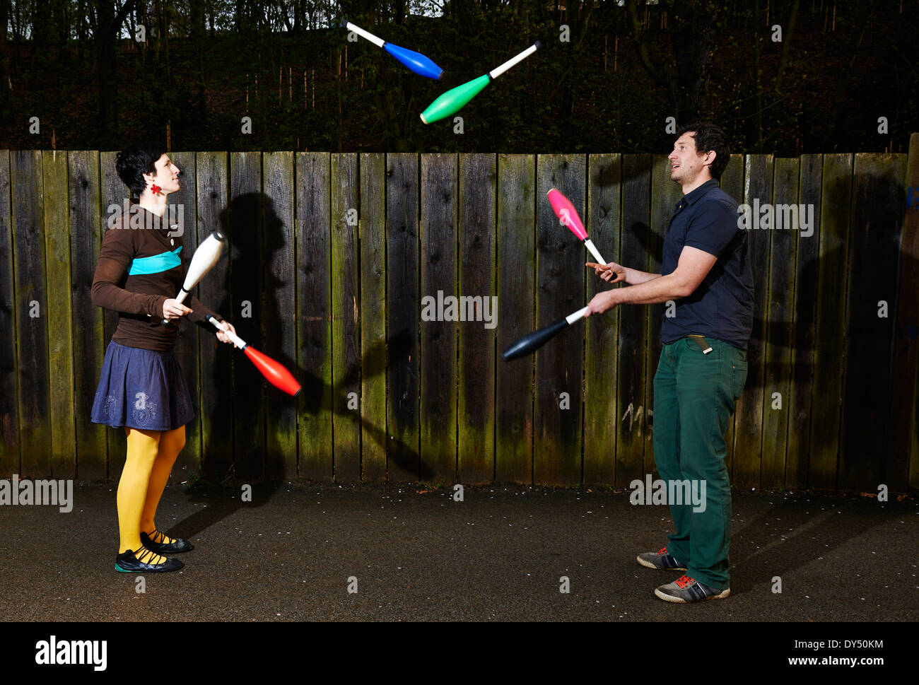 Zwei Personen Mann und Frau paar Jonglieren mit Keulen gegen die Holzwand im Park. Gaukler jonglieren Stockfoto