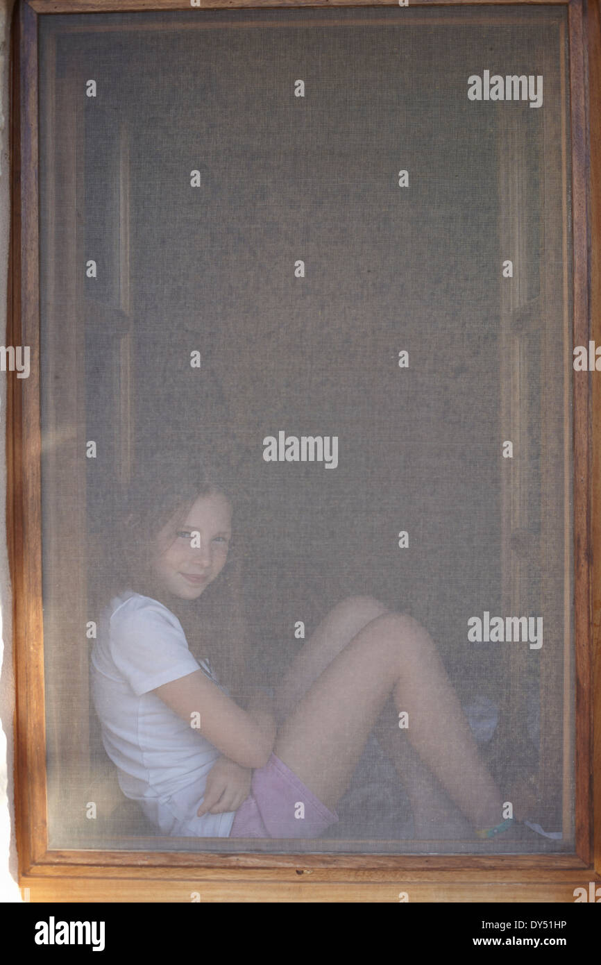 Porträt von Mädchen sitzen im Fensterrahmen verdeckt Stockfoto