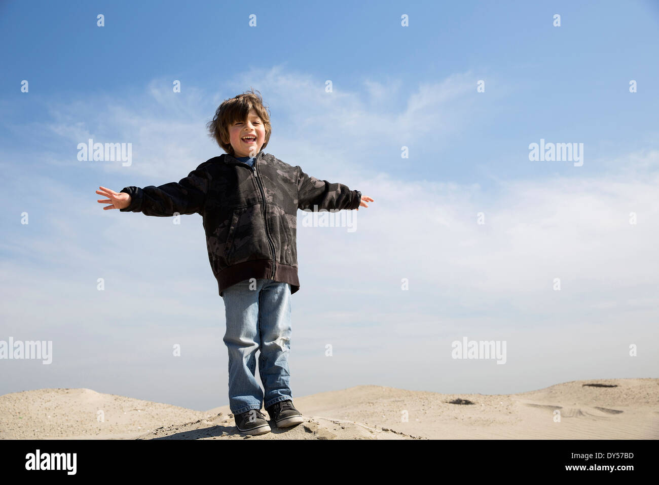 Lächelnde junge Stand auf Sand mit ausgestreckten Armen Stockfoto