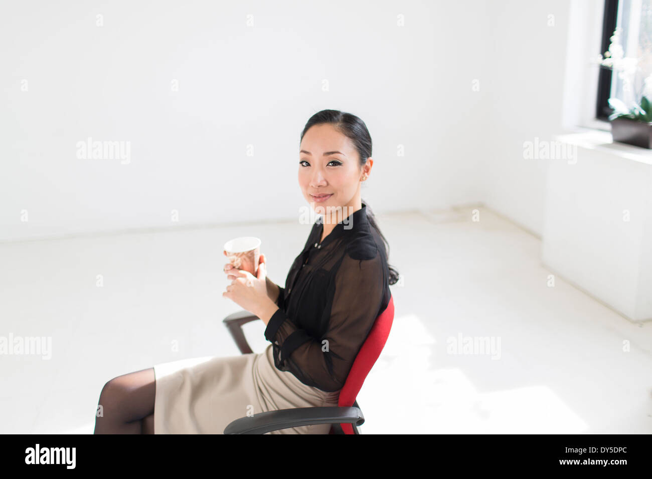 Junge Frau sitzt auf Bürostuhl mit Kaffee Stockfoto