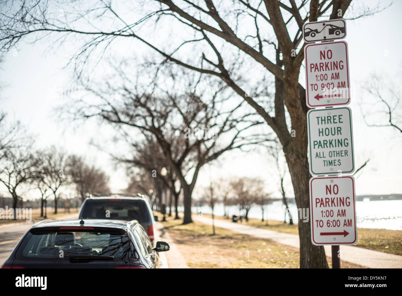 WASHINGTON DC, Vereinigte Staaten – mehrere Parkverbotsschilder sind vertikal auf einem Wegweiser entlang einer Washington DC Straße gestapelt. Auf der rechten Seite des Rahmens befinden sich parkende Autos, die die komplexe Parklandschaft in der Hauptstadt des Landes veranschaulichen. Stockfoto