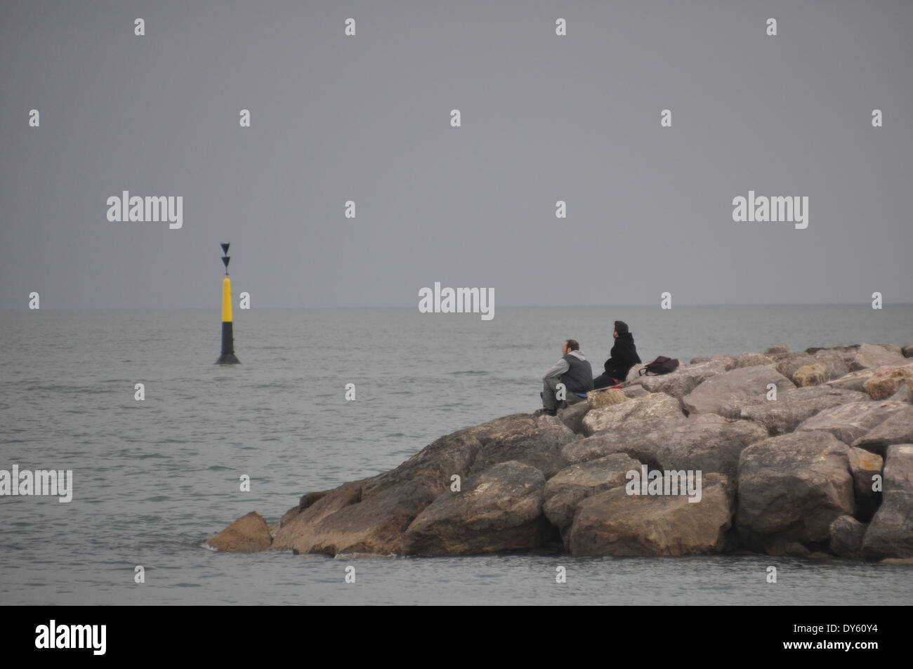 Ein paar sitzt am Ende auf eine Buhne, beobachten den Sonnenuntergang in Saintes Maries De La Mer, de Camargue, Frankreich Stockfoto