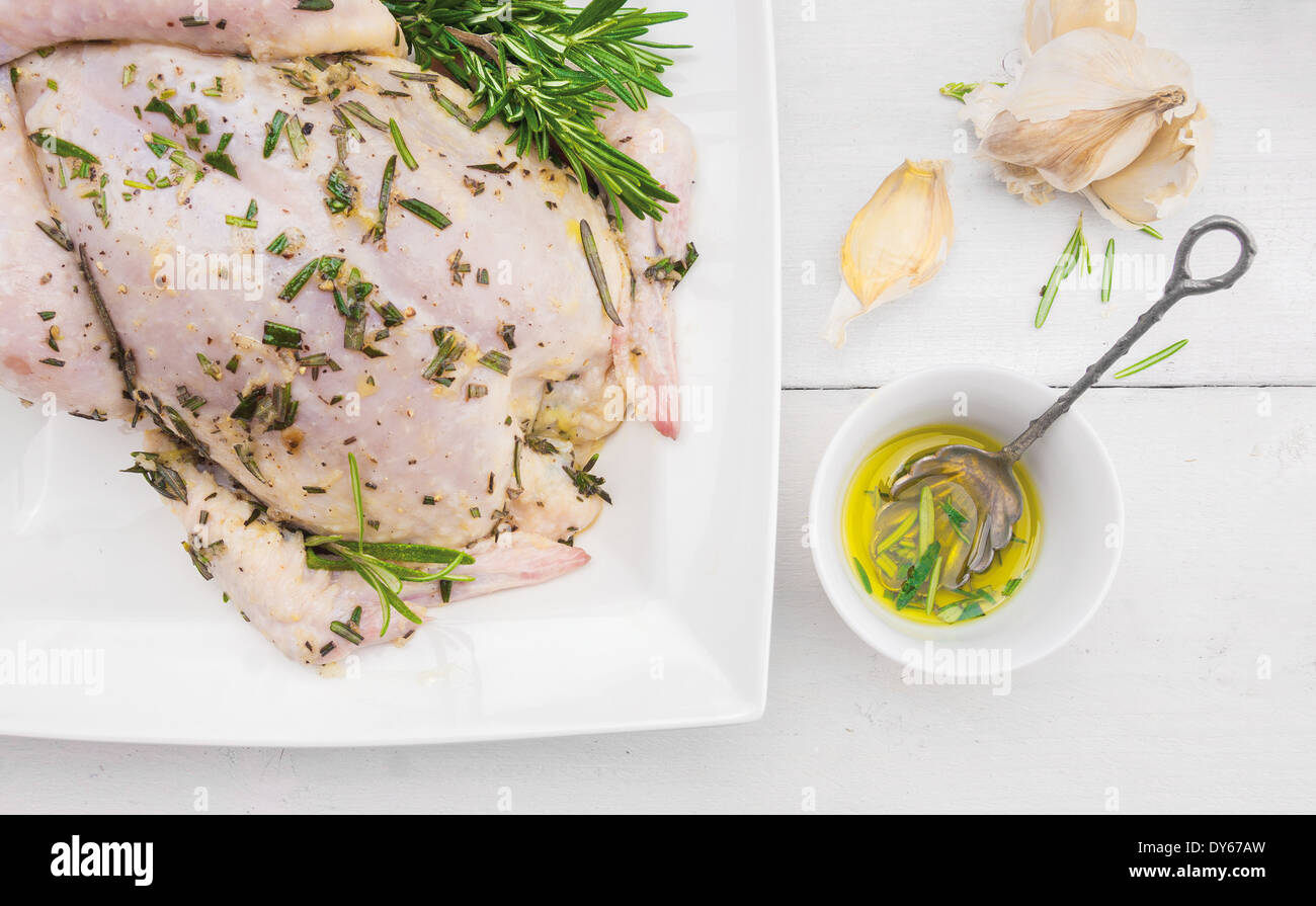 ganzes Huhn mit Olivenöl, Rosmarin und Knoblauch, Vorbereitung für Grill Braten auf weißer Holztisch Stockfoto