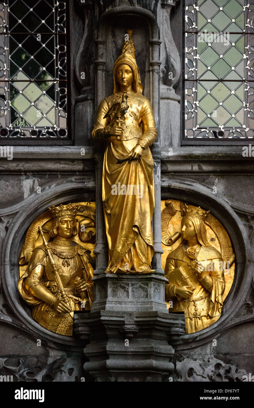 Basilika des Heiligen Blutes vergoldete Statue Brügge Belgien // BRÜGGE, Belgien — Eine vergoldete Statue, die eine Edelfrau mit einem Falken zeigt, ziert die Außenseite der Basilika des Heiligen Blutes auf dem Burgplatz. Dieses mittelalterliche Skulpturendetail kombiniert königliche Bilder mit Falknerei-Symbolik und spiegelt die kulturellen Traditionen des mittelalterlichen Adels wider. Die goldene Figur trägt zum aufwendigen gotischen Dekorationsprogramm der Basilika bei. Stockfoto