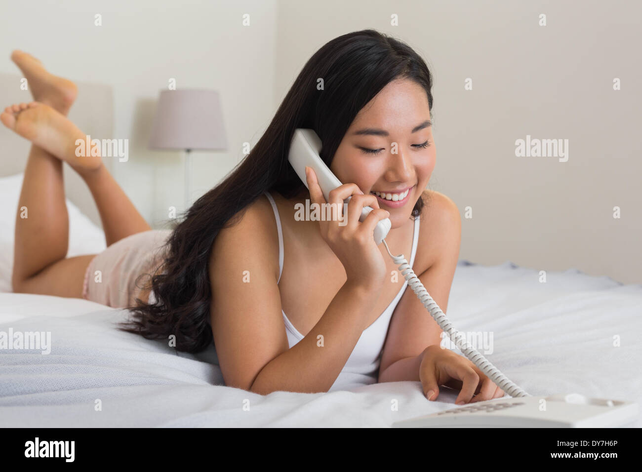 Glückliche Frau auf Bett mit Festnetz Telefon Stockfoto