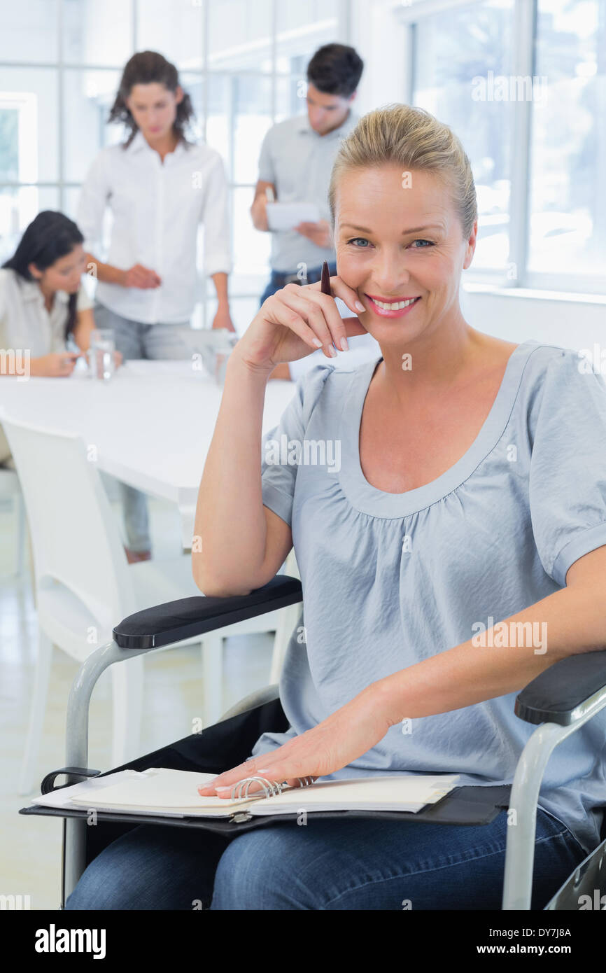 Lässige Geschäftsfrau im Rollstuhl lächelnd in die Kamera mit Team hinter ihr Stockfoto