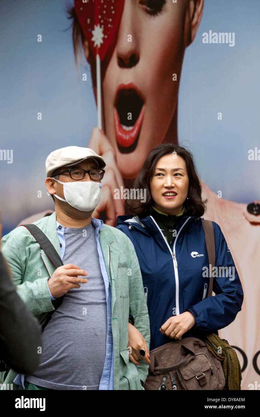 Asiatische Touristen mit Verschmutzungsmaske auf der Straße, Hinter ihnen Eine Werbetafel, Prag Tschechien Stockfoto