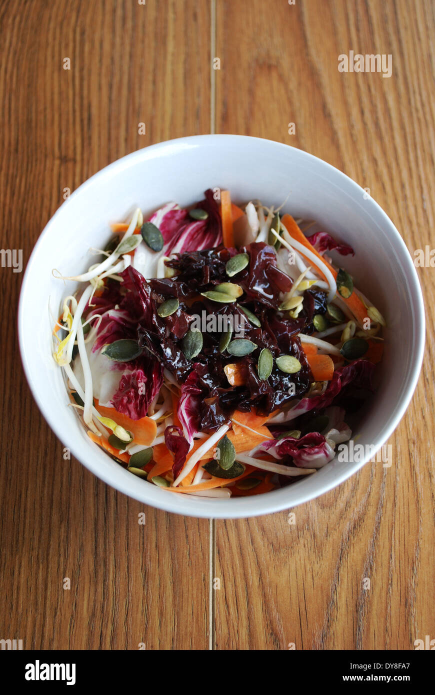 Roter Salat mit Karotten, Sprossen, Kürbiskerne und Algen in der Schüssel auf hölzernen Hintergrund weiß Stockfoto