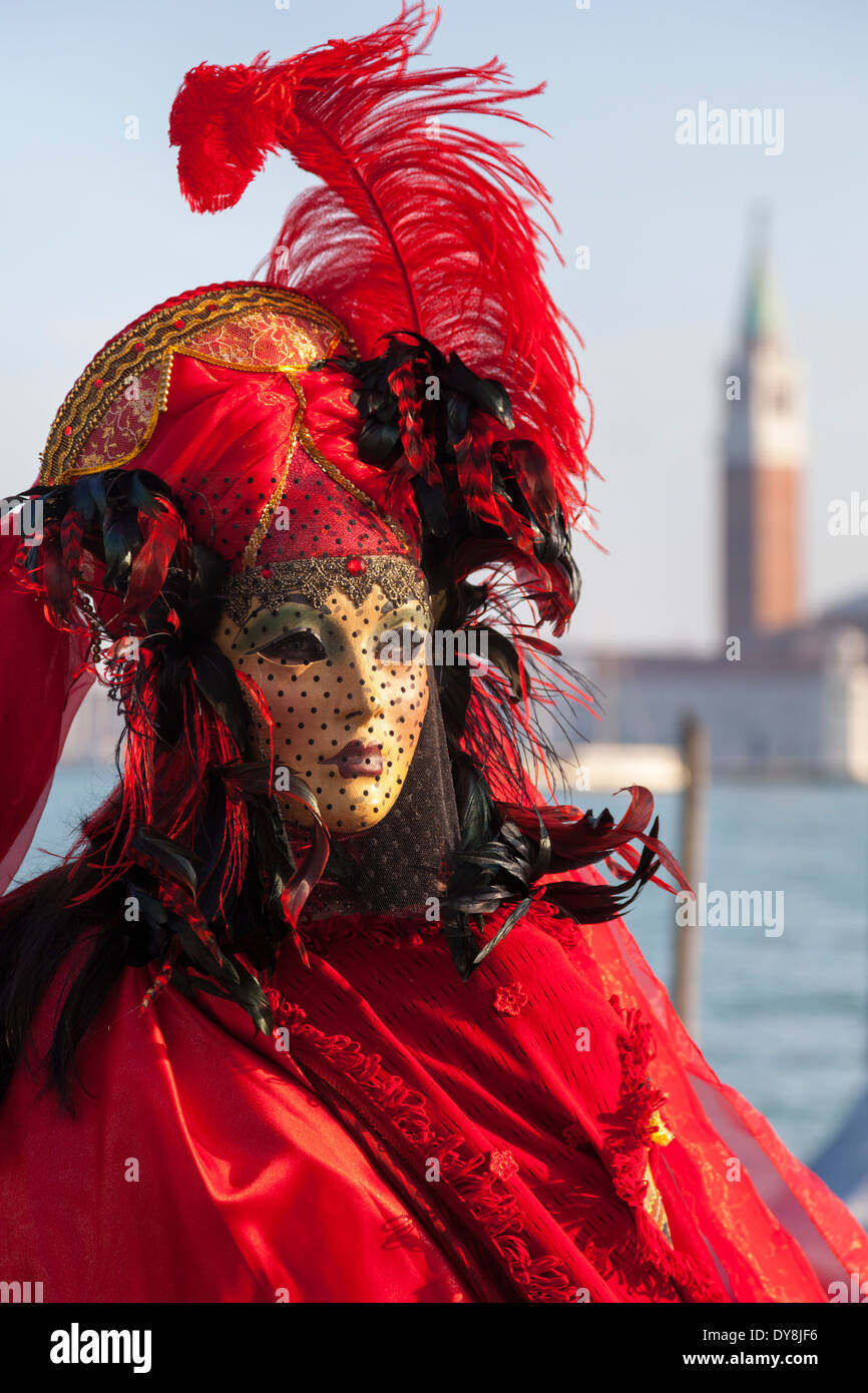 Karneval in Venedig, Frau in Maske, leuchtend rote Kostüm und gefiederte Hut posiert für Nahaufnahme während Carnevale di Venezia, Italien Stockfoto