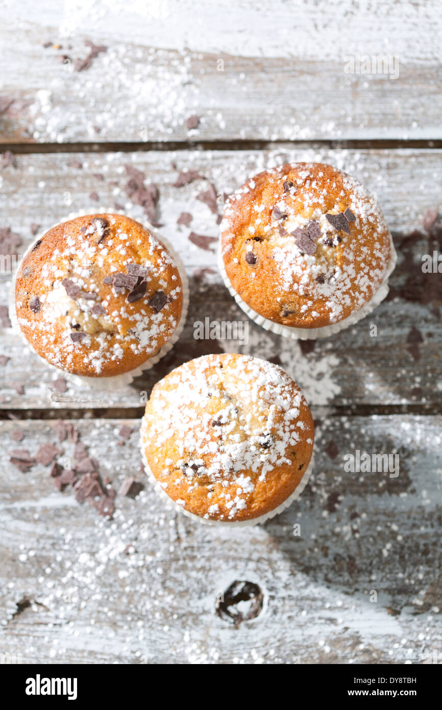 Drei Muffins in Pappbecher, bestreut mit Puderzucker und Schokoraspeln auf Holztisch, erhöhten Blick Stockfoto