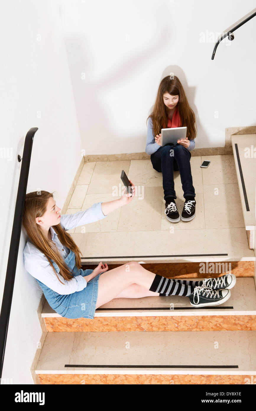 Zwei Mädchen im Teenageralter sitzen auf Treppen mit Smartphone und Tablet-digital Stockfoto