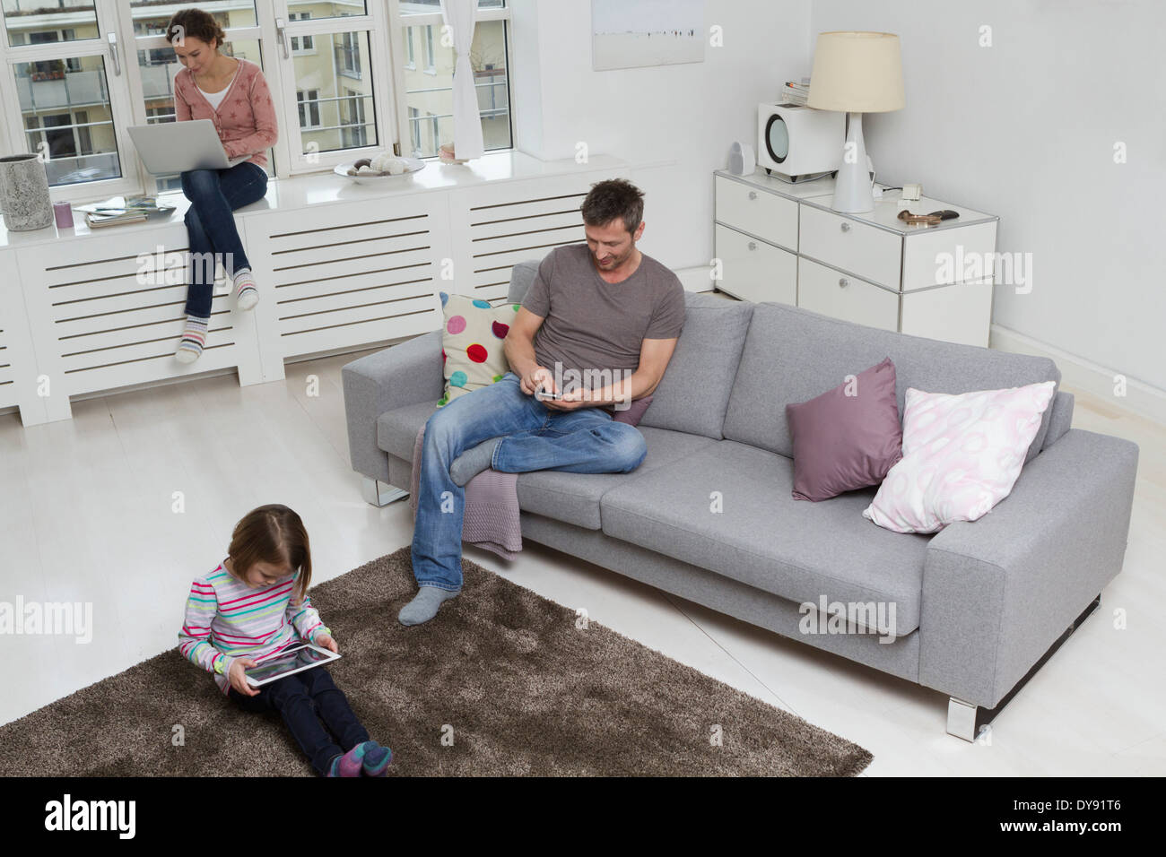 Mutter, Vater und Tochter, die mit tragbaren Geräten im Wohnzimmer Stockfoto