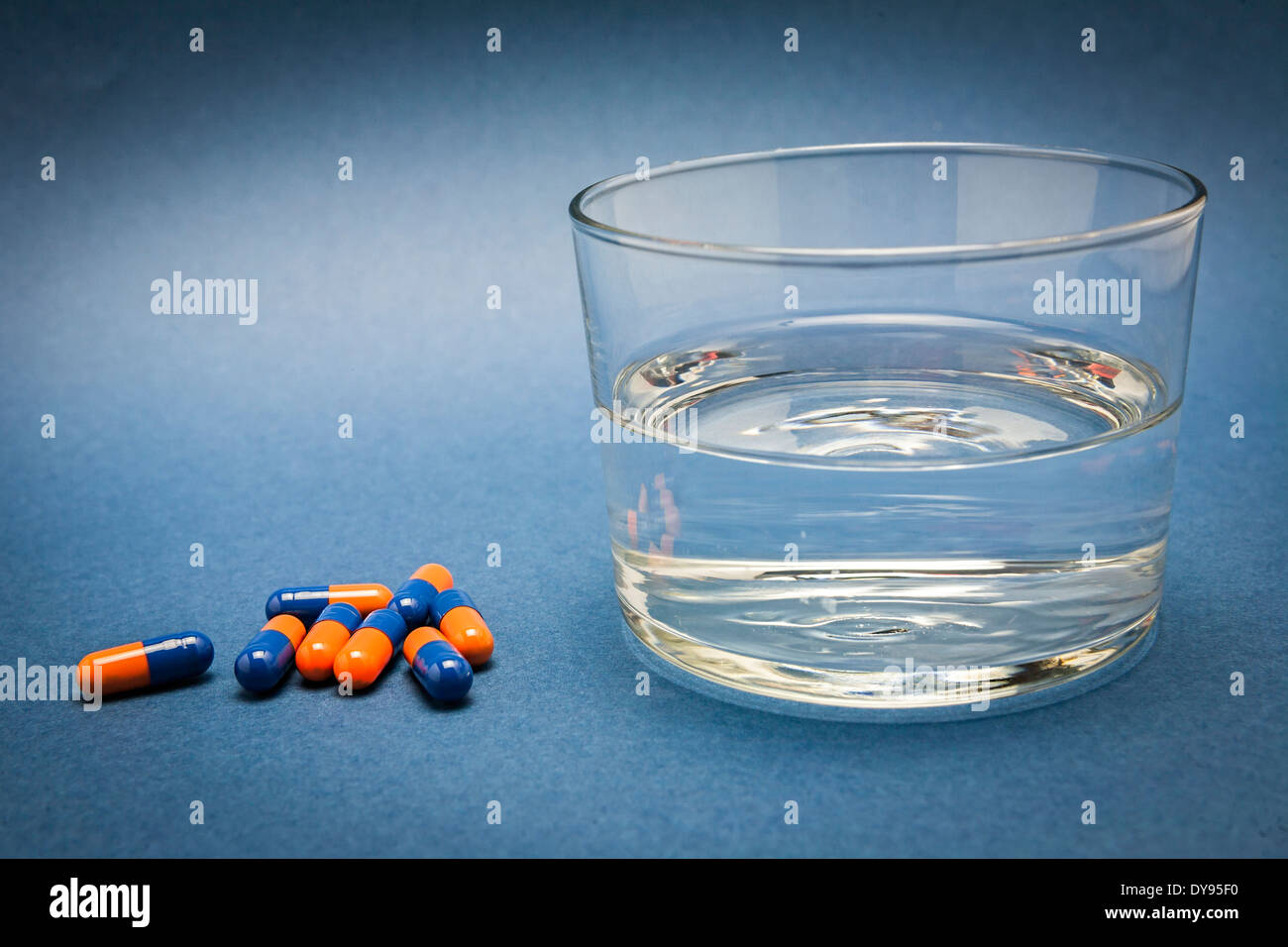 Glas Wasser und Pillen isoliert auf blau Stockfoto