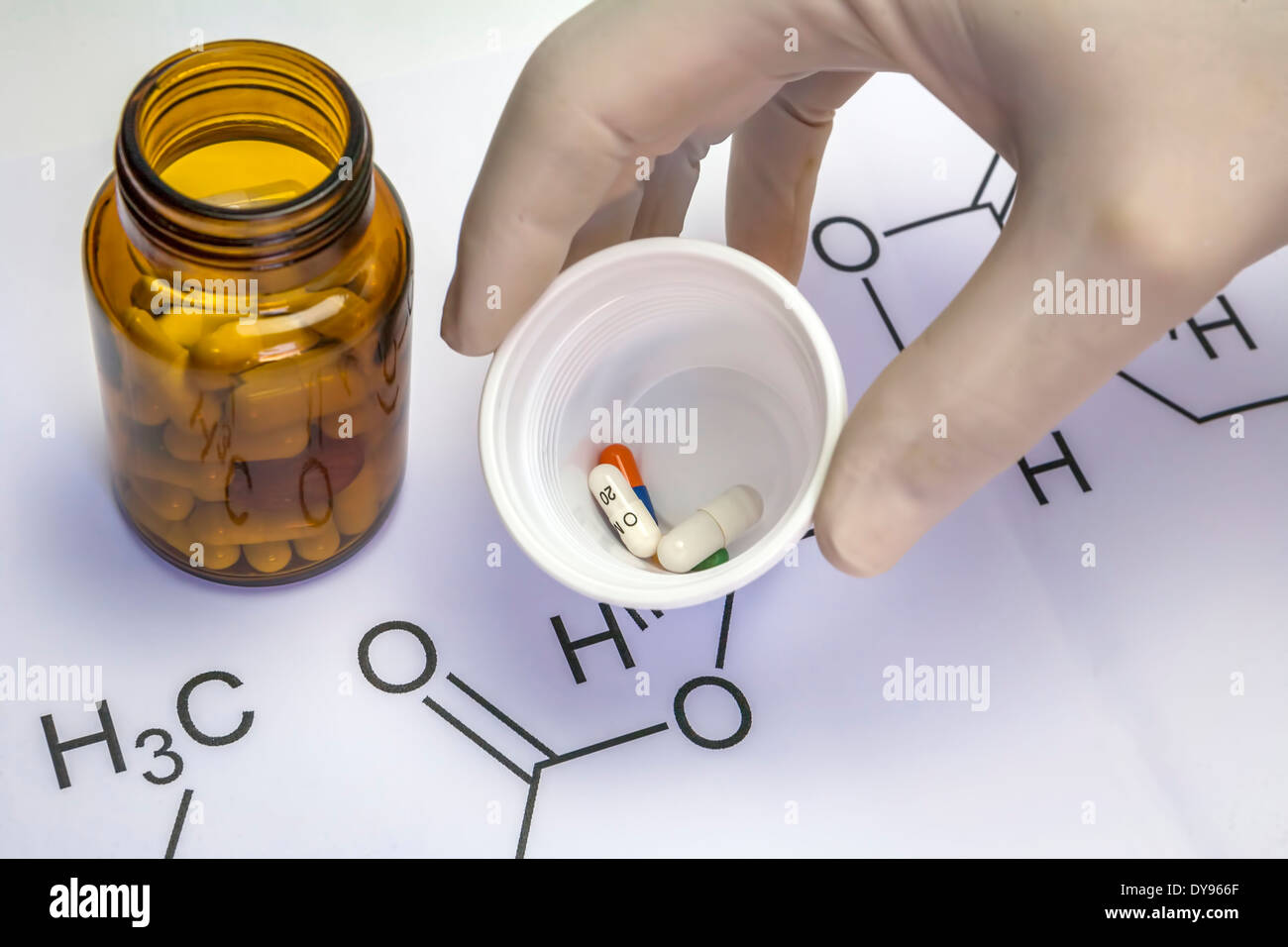 Chemie-Wissenschaft-Formel und Tabletten, Hand mit weißen Latex-Handschuh hält einen Plastikbecher mit mehreren Pillen Stockfoto