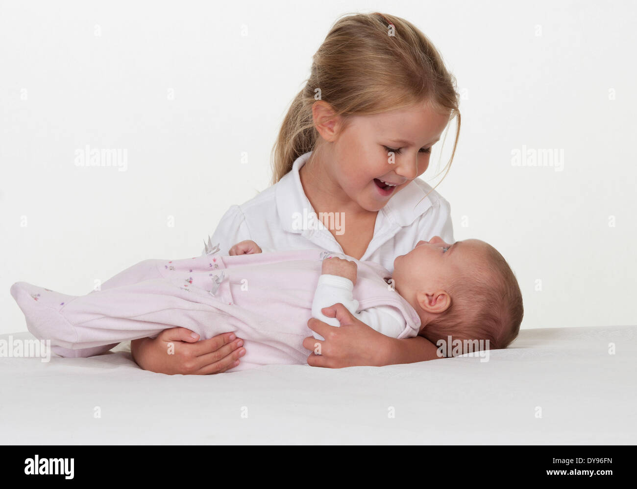 Kleines Mädchen hält Neugeborene Schwester lächelnd Stockfoto