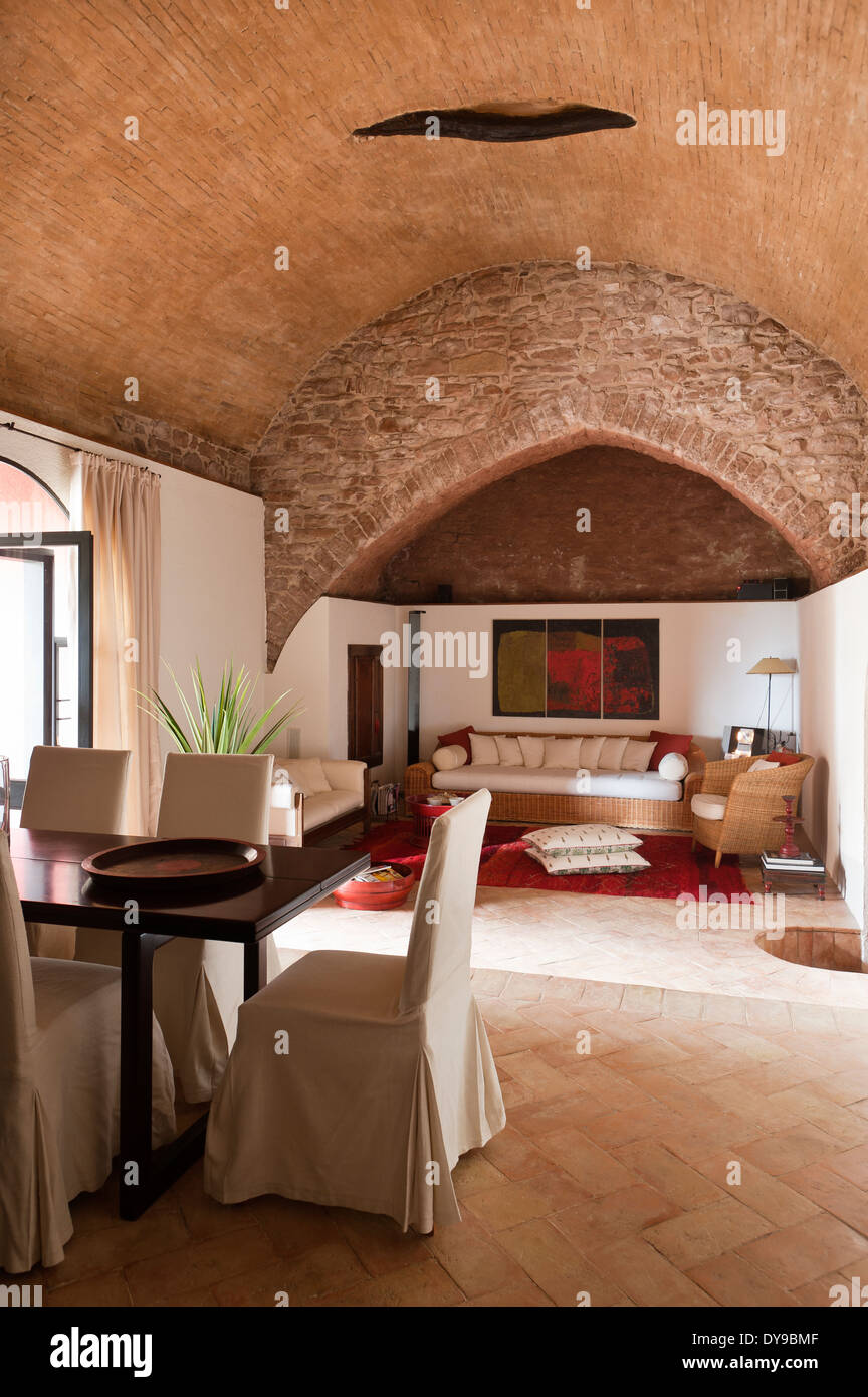 Offener Ess- und Wohnzimmer mit antiken Steinbogen. Die Esszimmerstühle sind mit roher Seide bedeckt. Stockfoto