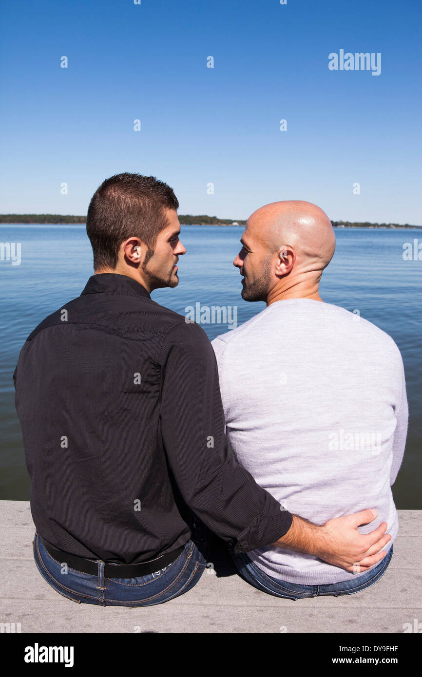 Zwei schwule Männer umarmen und teilen einige intime Momente auf einem Steg am See an einem sonnigen Nachmittag Frühjahr/Sommer/Herbst. Stockfoto