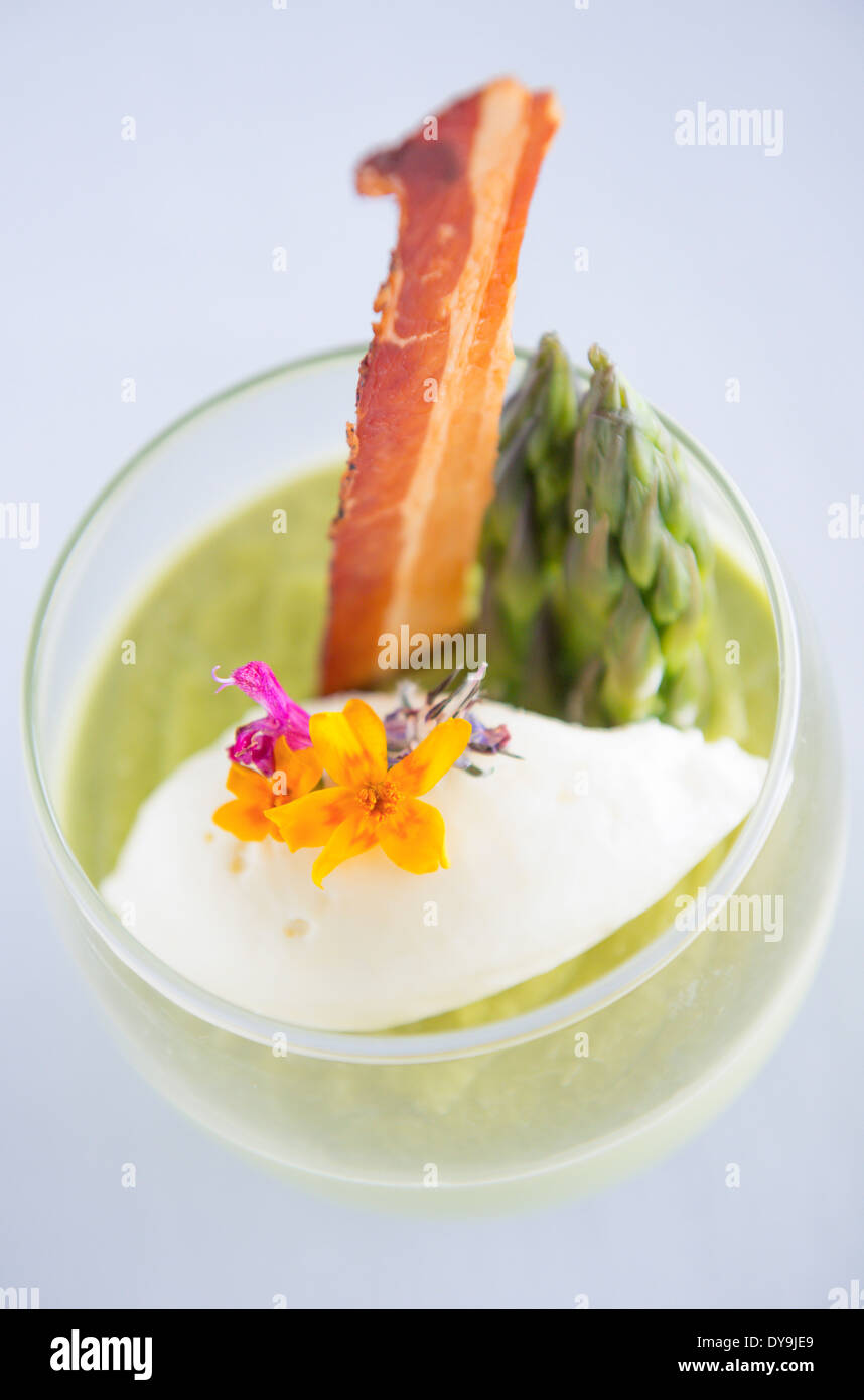 Spargelsuppe serviert in einem Glas mit Speck, Spargelspitzen und Blumen geschmückt. Stockfoto