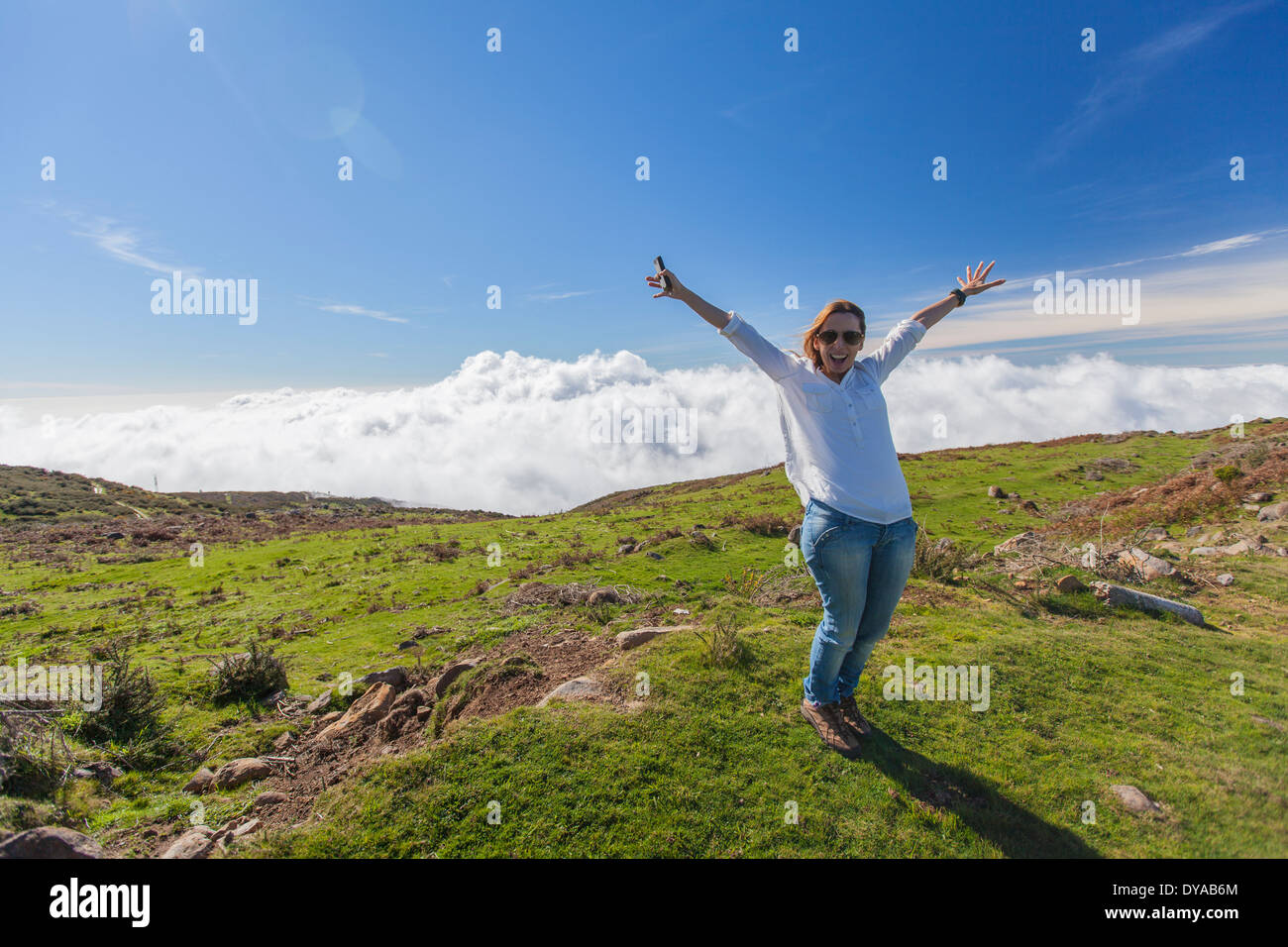 Glückliche Frau auf einem Berg mit Wolken unter Stockfoto