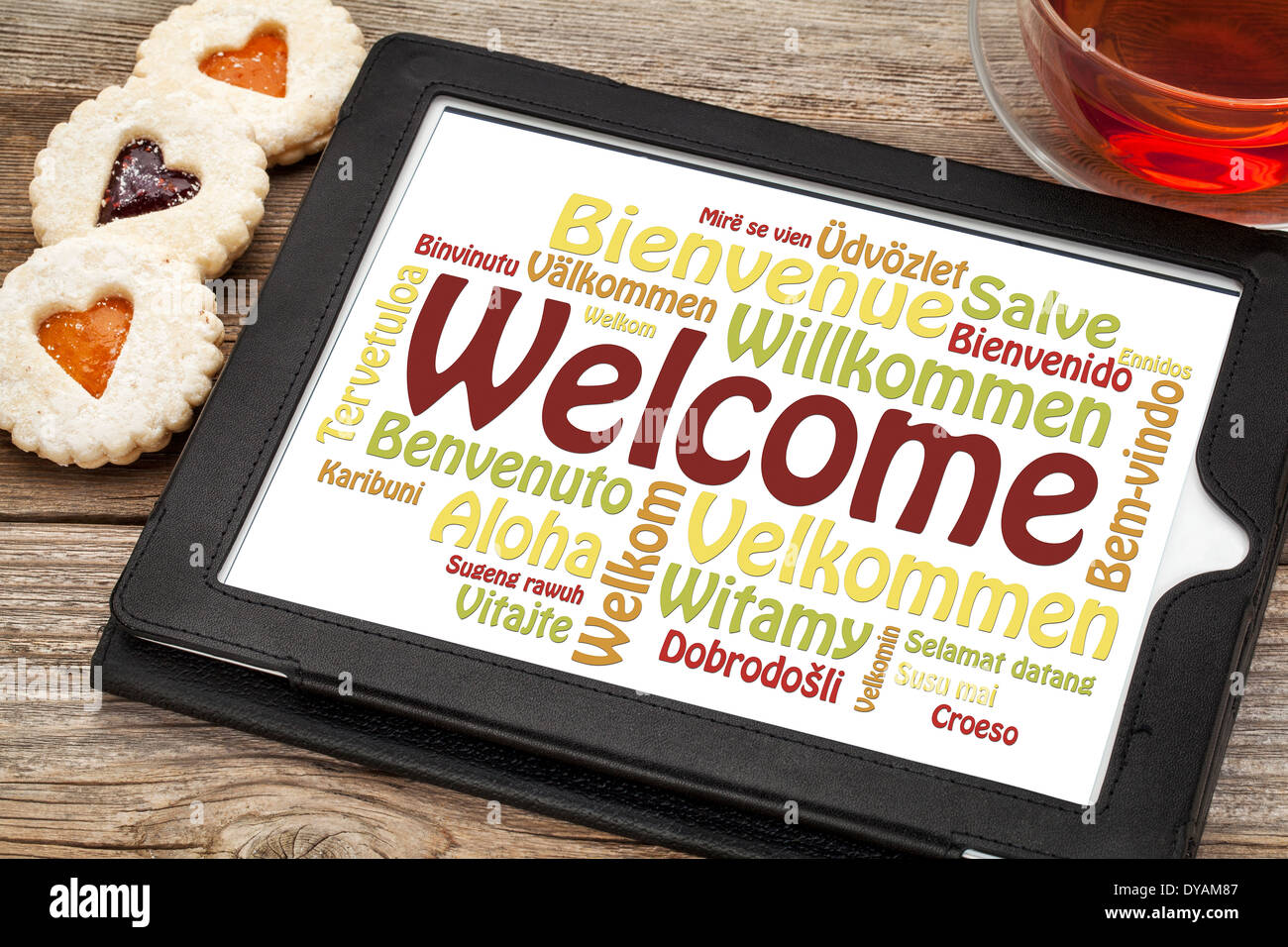 Willkommen Wortwolke in verschiedenen Sprachen auf einem digitalen Tablet mit einer Tasse Tee und Cookies Herz Stockfoto