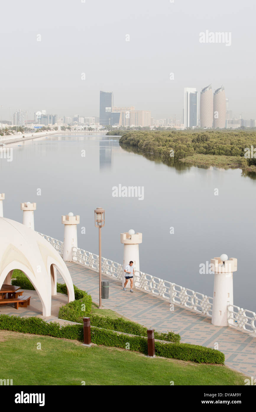 Ein Mann läuft auf einen Gang durch den Park entlang der Al Salam Street und die Mangroven mit der Stadt Abu Dhabi im Hintergrund. Stockfoto