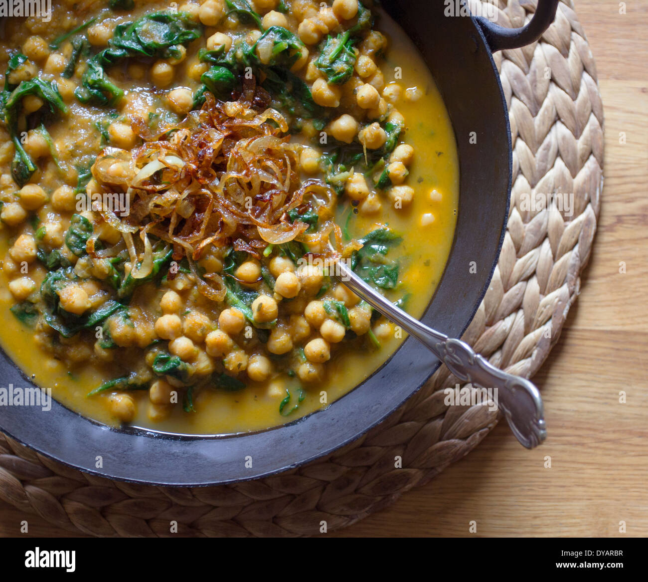 Kichererbsen und Spinat curry mit karamellisierten Zwiebeln in einem gusseisernen Kochtopf auf einen Eichentisch Stockfoto