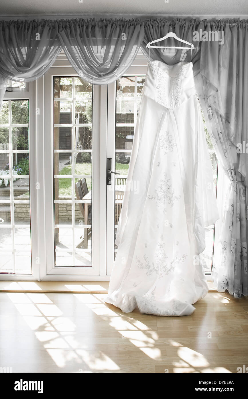 weiße Brautkleid von einer Gardinenstange hängen mit der Sonne durch das Fenster, Stockfoto