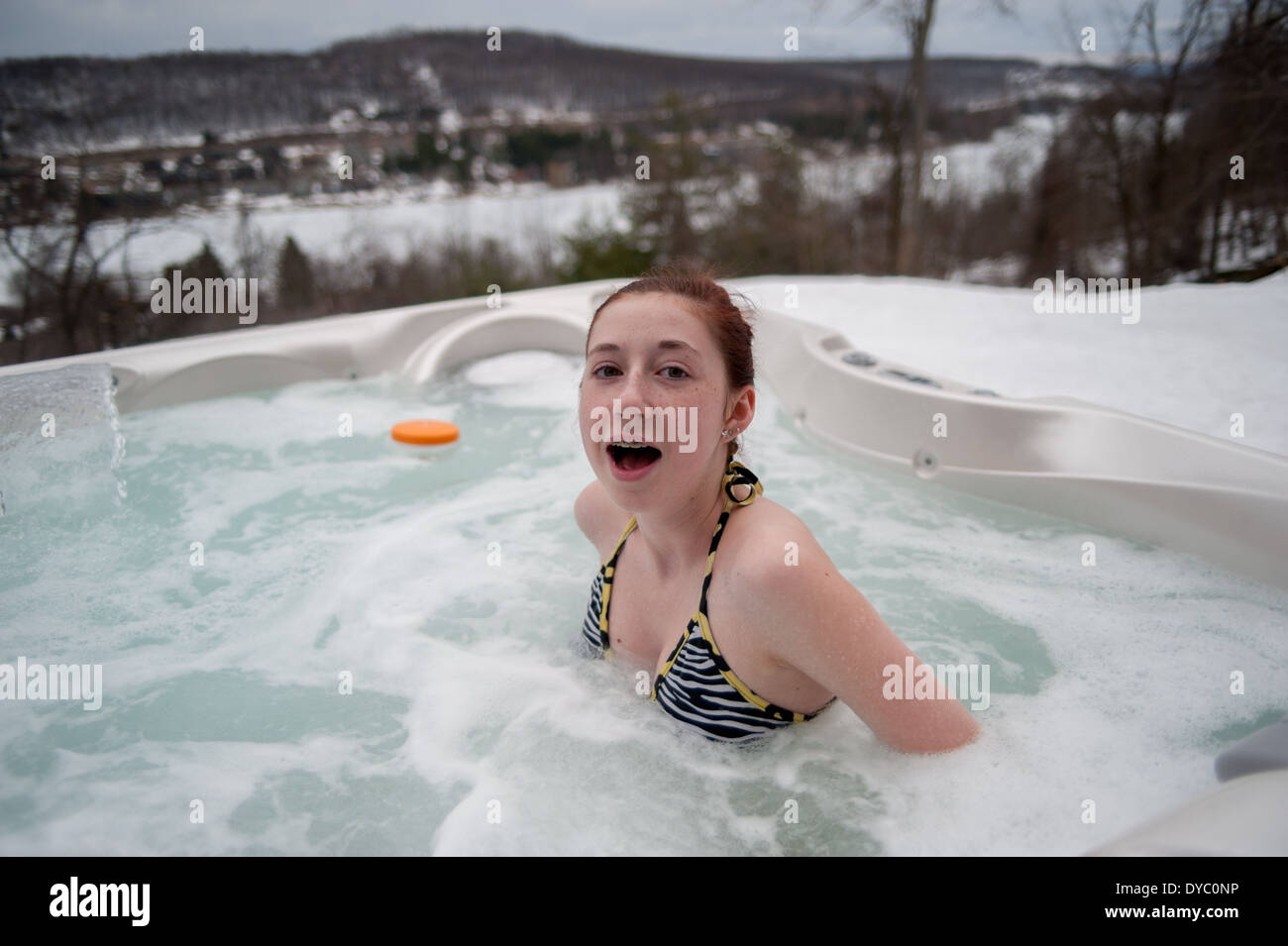 Teenager-Mädchen schockiert durch die Warmwassertemperatur im Whirlpool in verschneiten Bergen Stockfoto