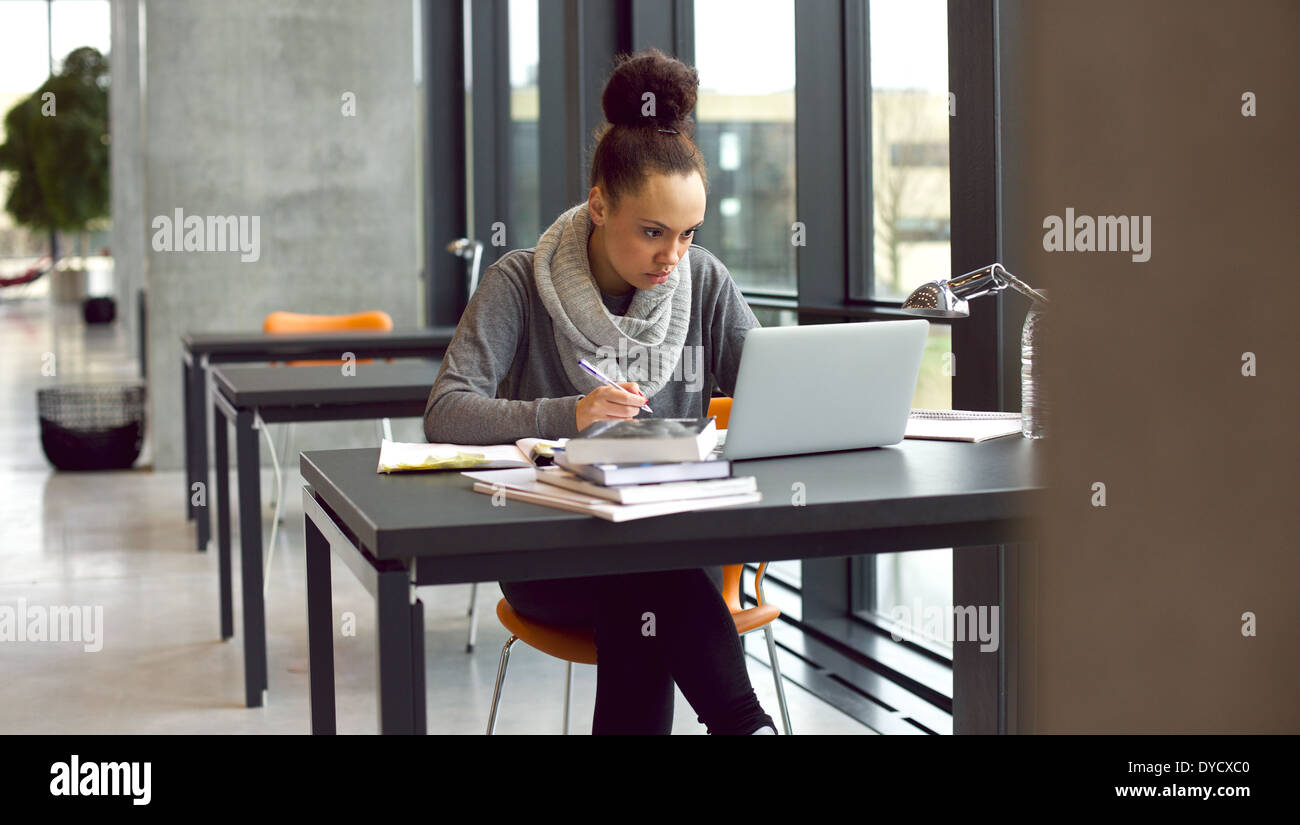 Junge Afro Amerikanerin sitzen am Tisch mit Büchern und Laptop zum Auffinden von Informationen. Junger Student Notizen von laptop Stockfoto