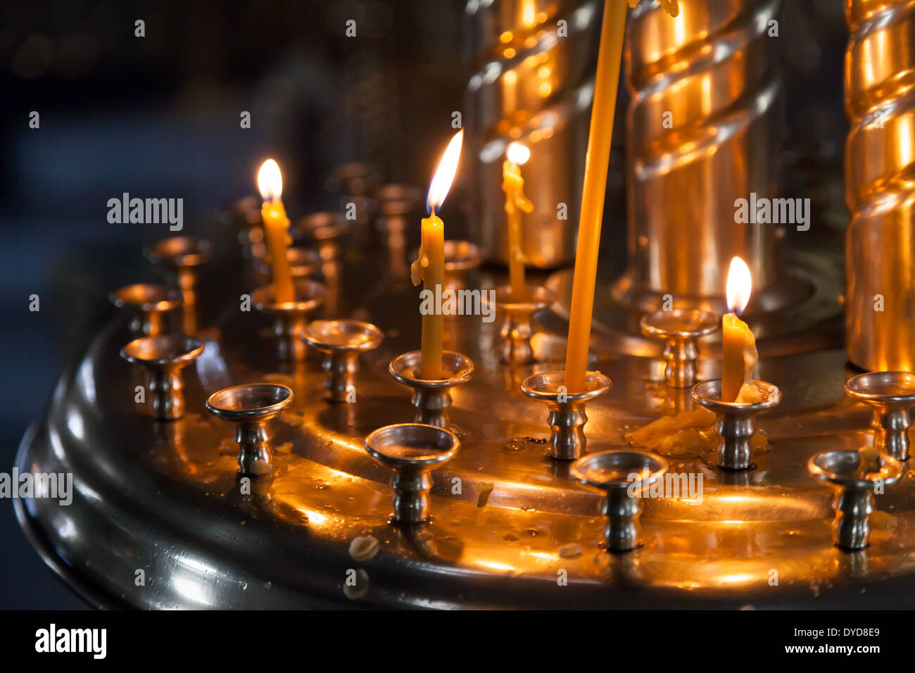 In einer dunklen orthodoxen Kirche werden kleine Kerzen angezündet. Stockfoto