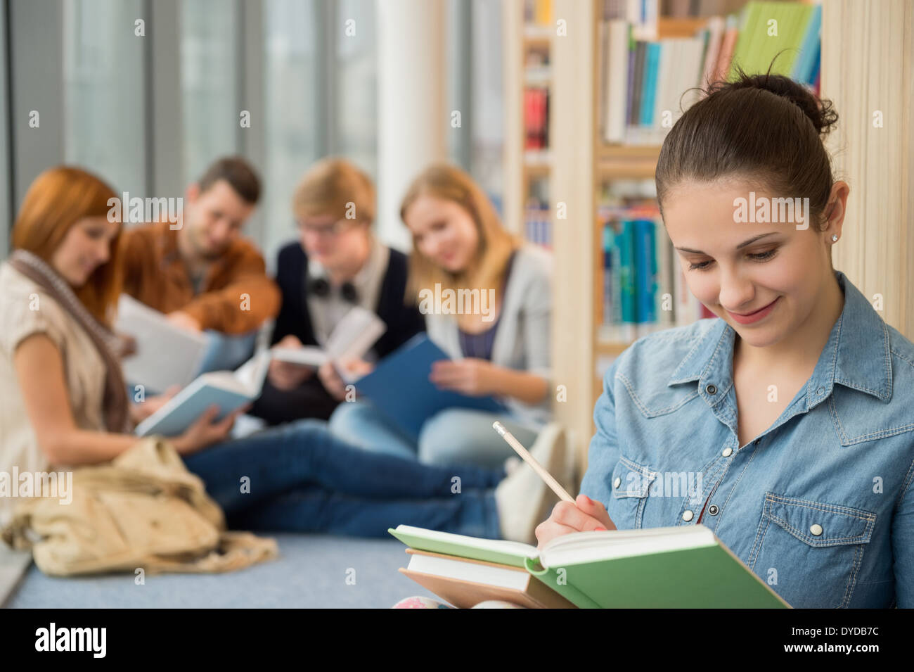 Junge Schule studiert mit Freunden im Hintergrund in Bibliothek Stockfoto