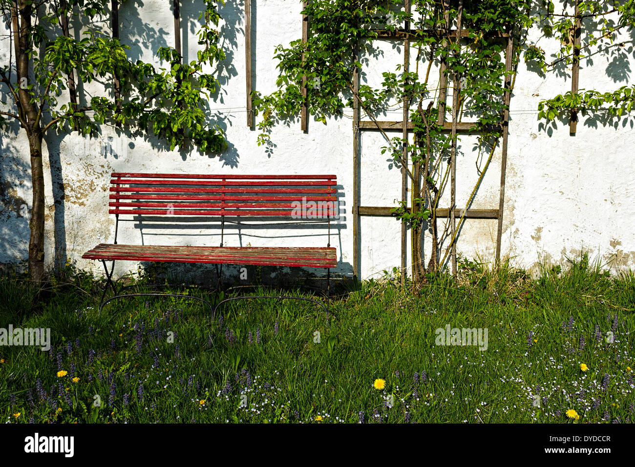 Alte rote Holz Sitzbank gegen weiße Wand im Garten, Oberbayern, Deutschland, Europa. Stockfoto