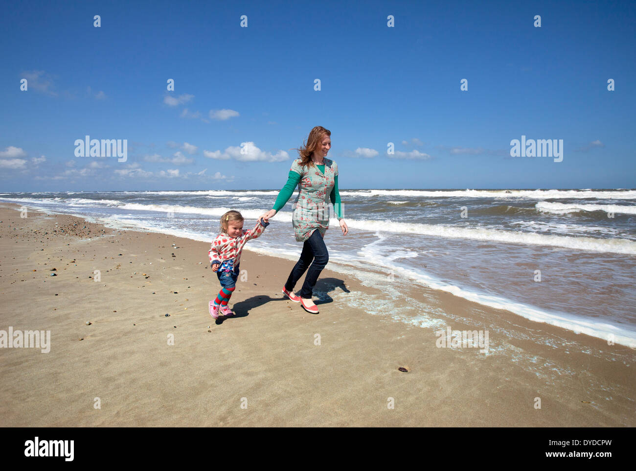 Eine Mutter und Tochter läuft am Horsey Strand an der Küste von Norfolk. Stockfoto