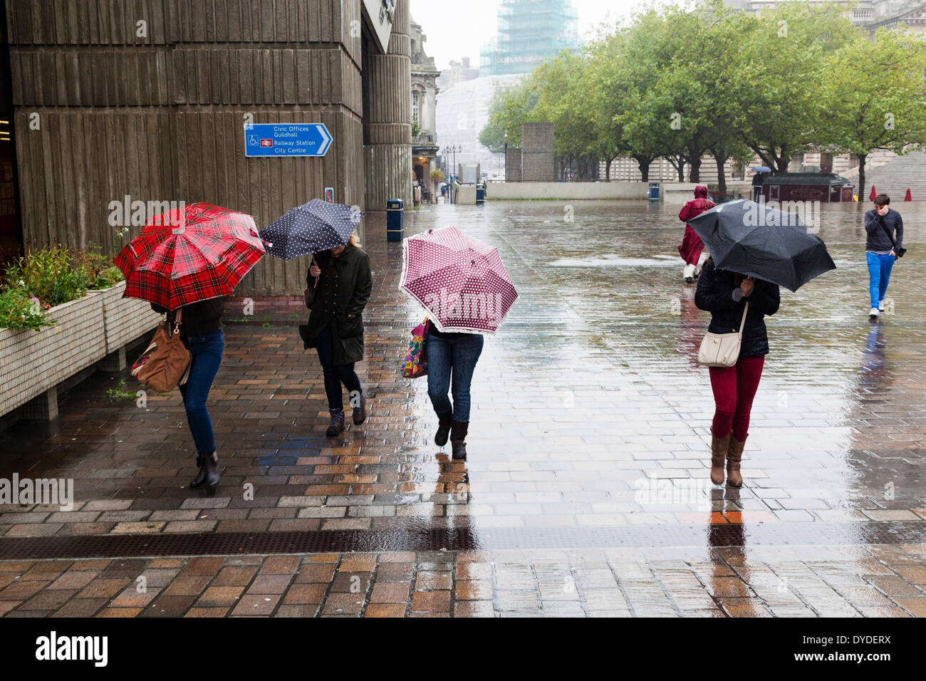 Vier Frauen mit Sonnenschirmen mit Kopf nach unten gegen den Wind und Regen. Stockfoto