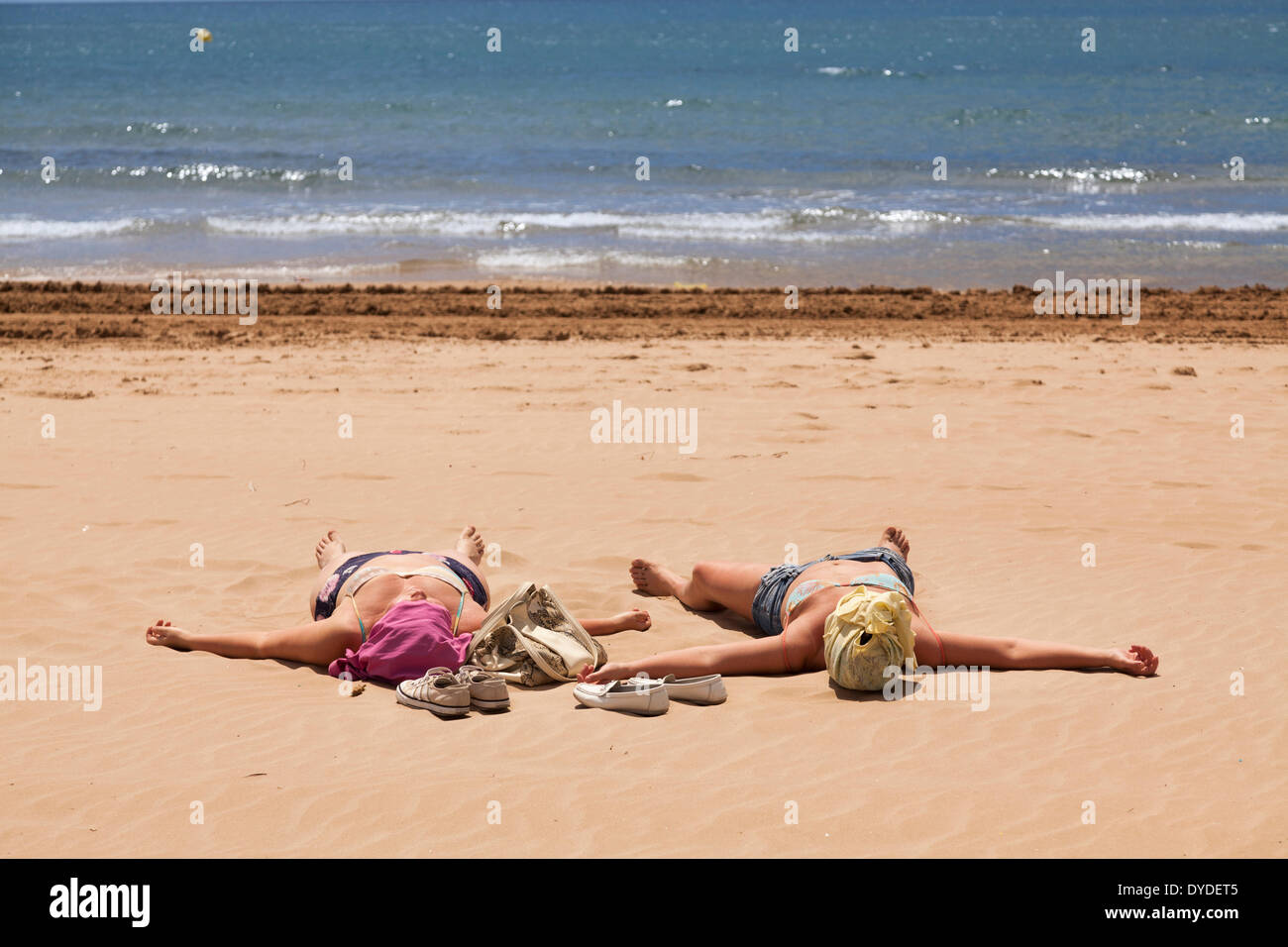 Zwei Frauen mit überdachten Köpfe spreadeagle am Strand Sonnenbaden. Stockfoto