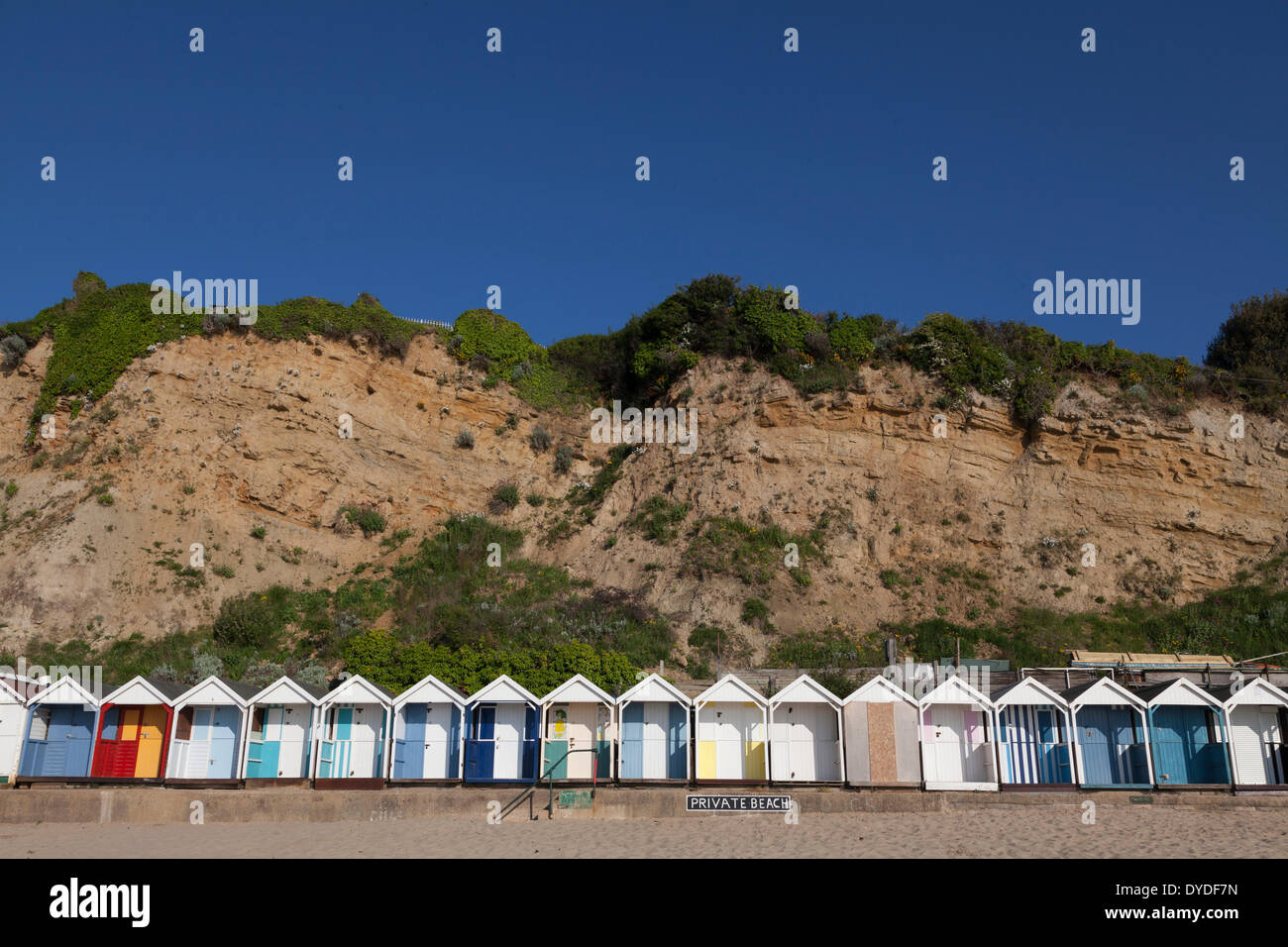 Reihe von hellen Strandhütten unter dem Felsen am Strand von Swanage. Stockfoto