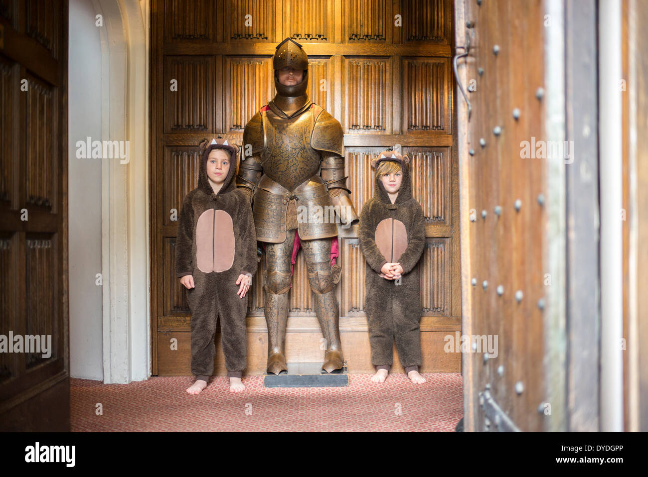 Zwei Jungs in Onesies stand neben einem Ritter in Rüstung in Thornbury Castle. Stockfoto