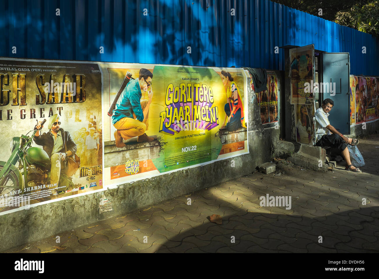 Ein Telefon-Mechaniker nimmt Auszeit an eine offene Anschlussdose entlang einer Wand anzeigen Bollywood Movie Poster. Stockfoto