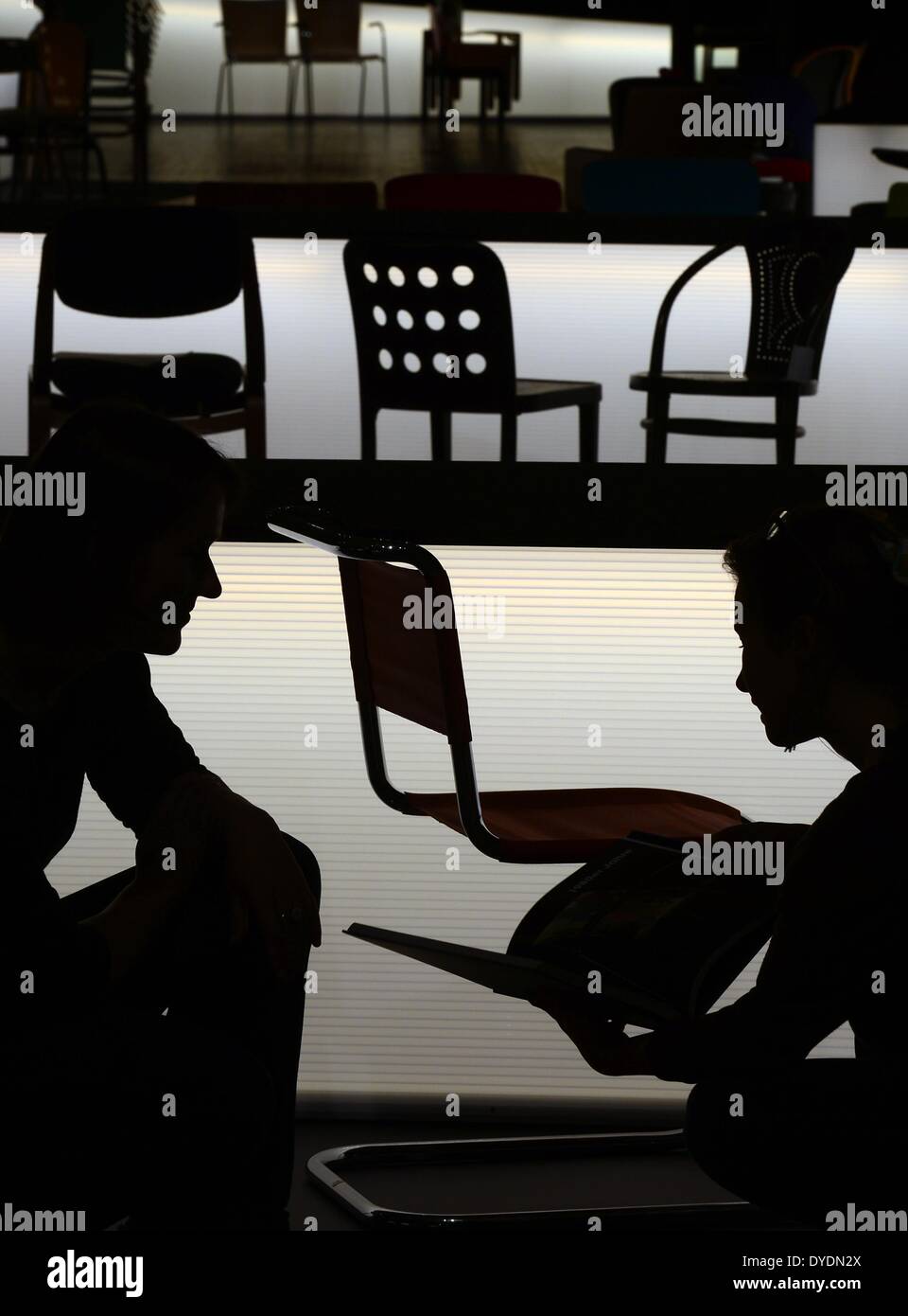 Leipzig, Deutschland. 15. April 2014. Zwei Frauen und mehrere Stühle der Firma Thonet sind gegen beleuchtete Tische im Grassi Museum für angewandte Kunst in Leipzig, Deutschland, 15. April 2014 Silhouette. Die Thonet-Ausstellung "Sitzen - liegen - Rock" zeigt über 130 historische Stühle und Designklassiker des Unternehmens aus dem Bundesland Hessen und läuft von 17 April bis 14. September 2014. Foto: Hendrik Schmidt/Dpa/Alamy Live News Stockfoto