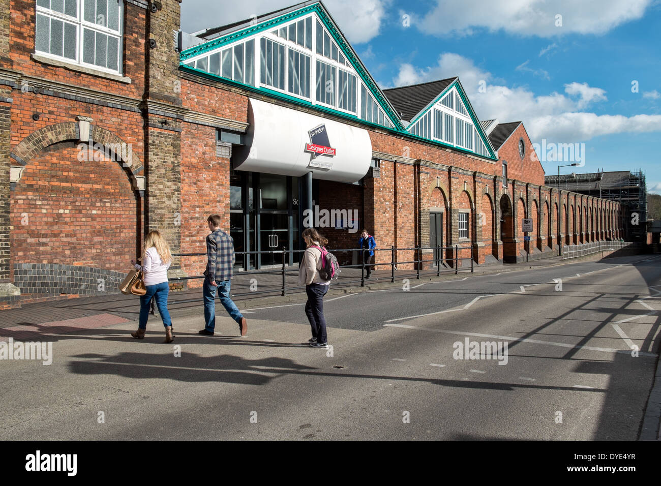 Menschen, die zu Fuß in Richtung der Zeichen & Eingang für das McArthur Glen Designer Outlet Village in Swindon, Wiltshire, UK an einem sonnigen Tag Stockfoto