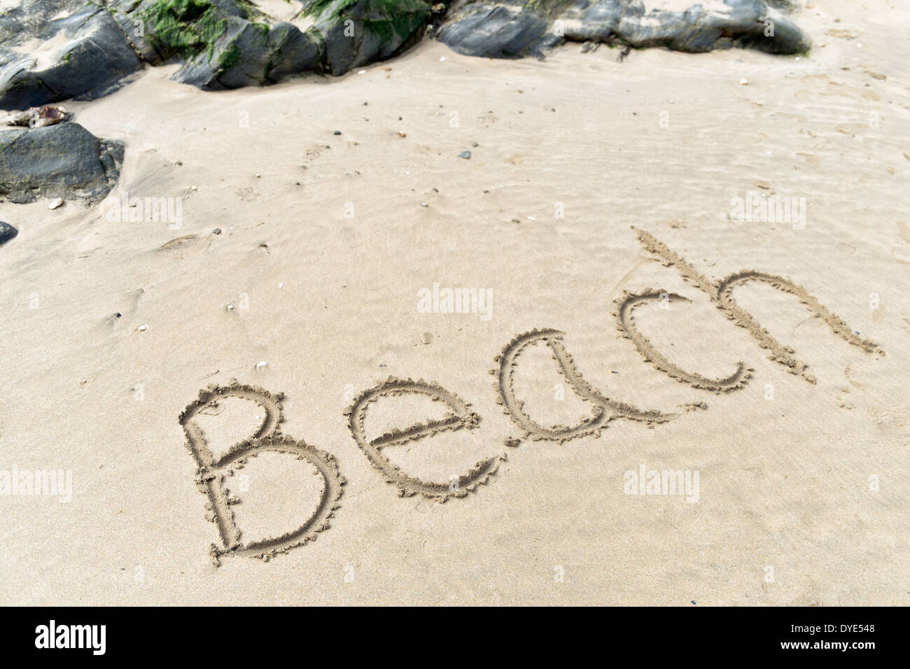 Großen Buchstaben den Wort Strand in den Sand geschrieben, von Felsen auf einem sonnigen, sandigen Ufer mit Stockfoto