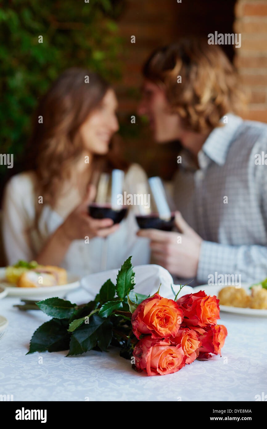 Ein Strauß roter Rosen auf bedienten Tisch und junge Liebende, toasten auf Hintergrund Stockfoto