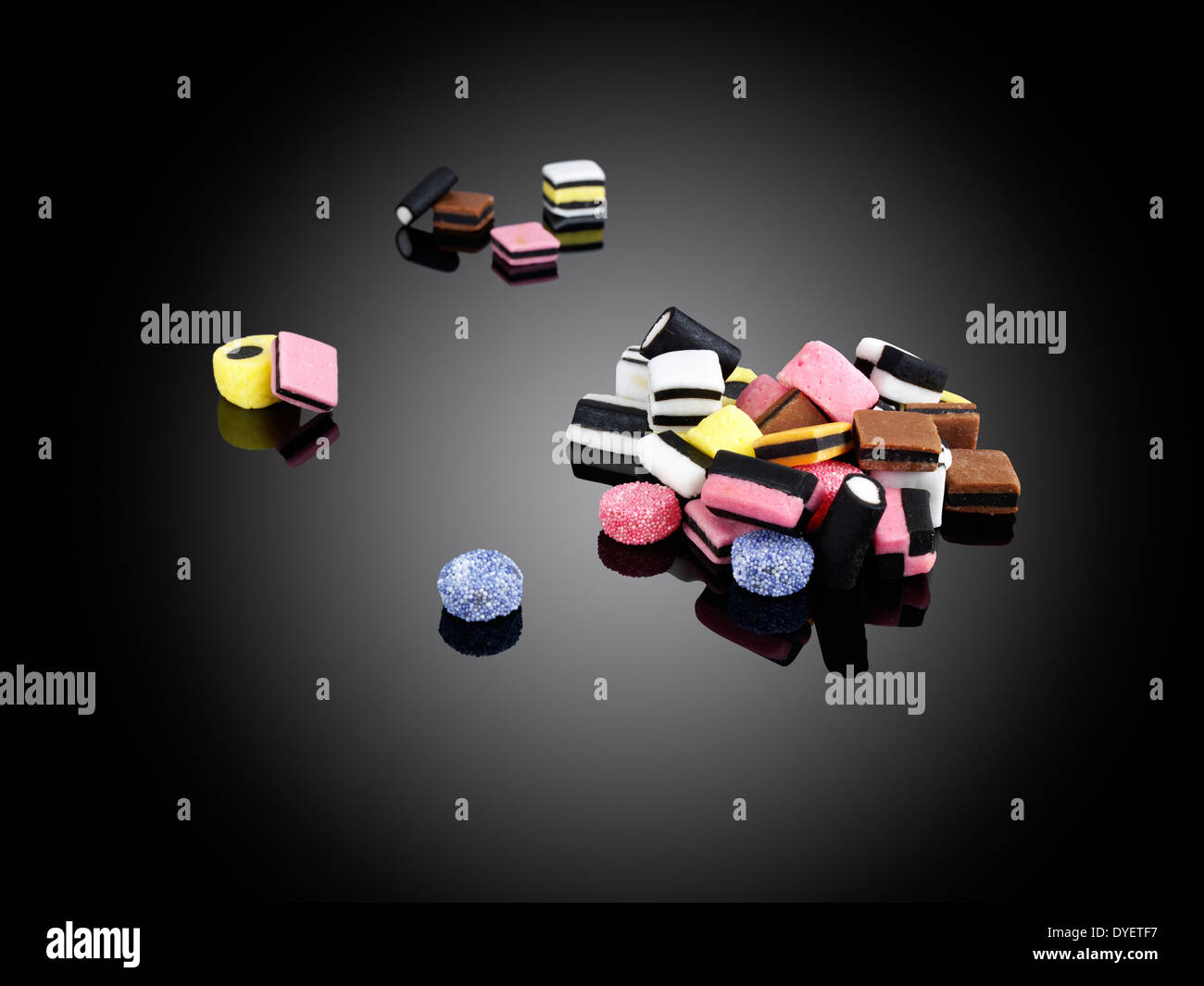EINE STREUUNG DER LIQUORICE ALLSORTS AUF REFLEKTIERENDE VIELFARBIG SCHWARZEN HINTERGRUND Stockfoto