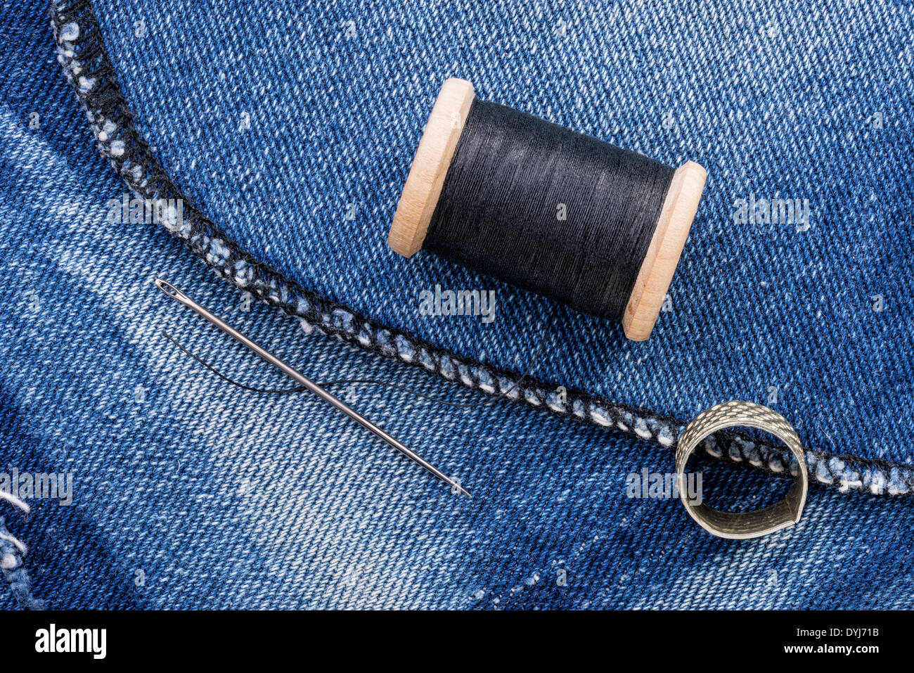 Eine Rolle von schwarzen Faden und eine Nadel auf einem Stück von Blue Jeans denim Stockfoto